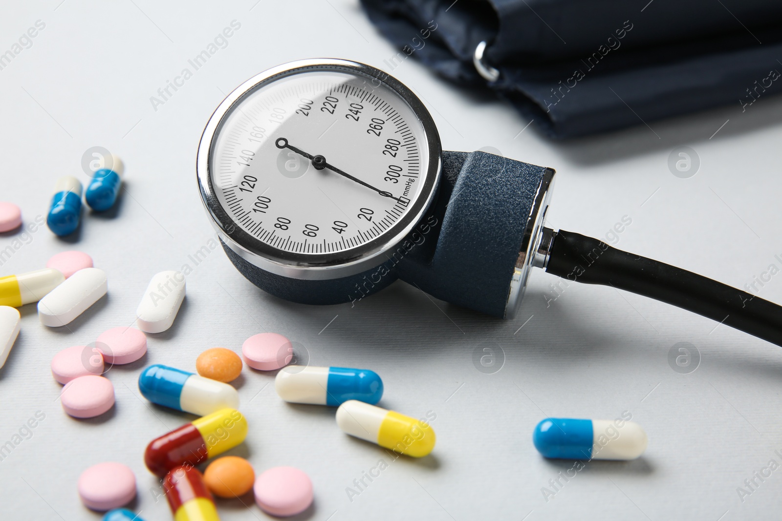 Photo of Blood pressure measuring device and pills on light grey background, closeup