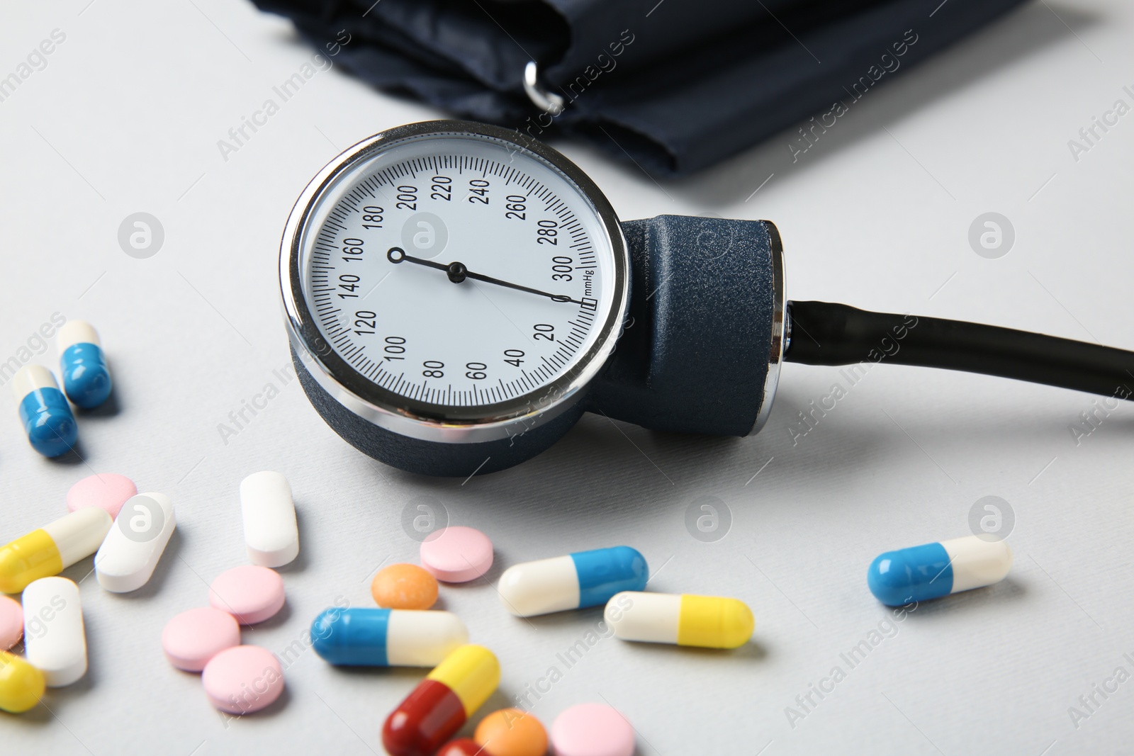 Photo of Blood pressure measuring device and pills on light grey background, closeup