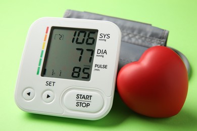 Photo of Blood pressure measuring device and squeeze heart on green background, closeup