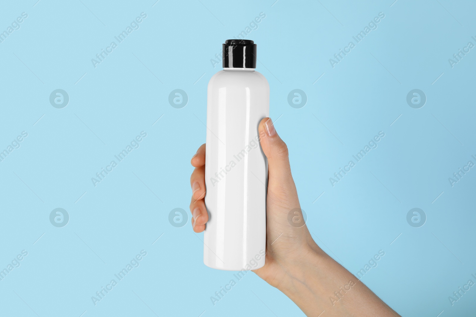 Photo of Woman with shampoo bottle on light blue background, closeup