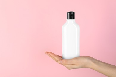 Photo of Woman with shampoo bottle on pink background, closeup. Space for text