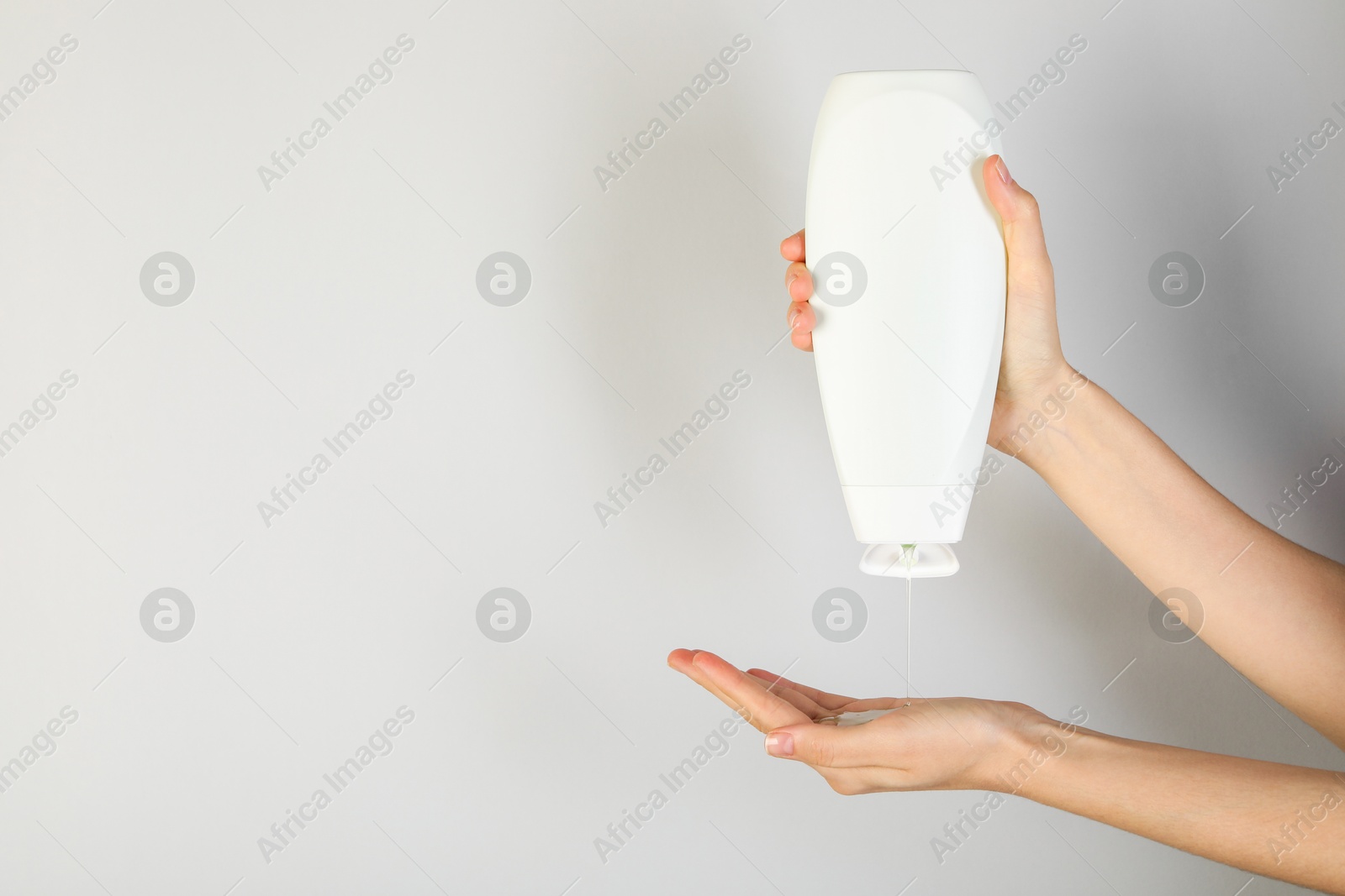 Photo of Woman pouring shampoo onto hand on grey background, closeup. Space for text