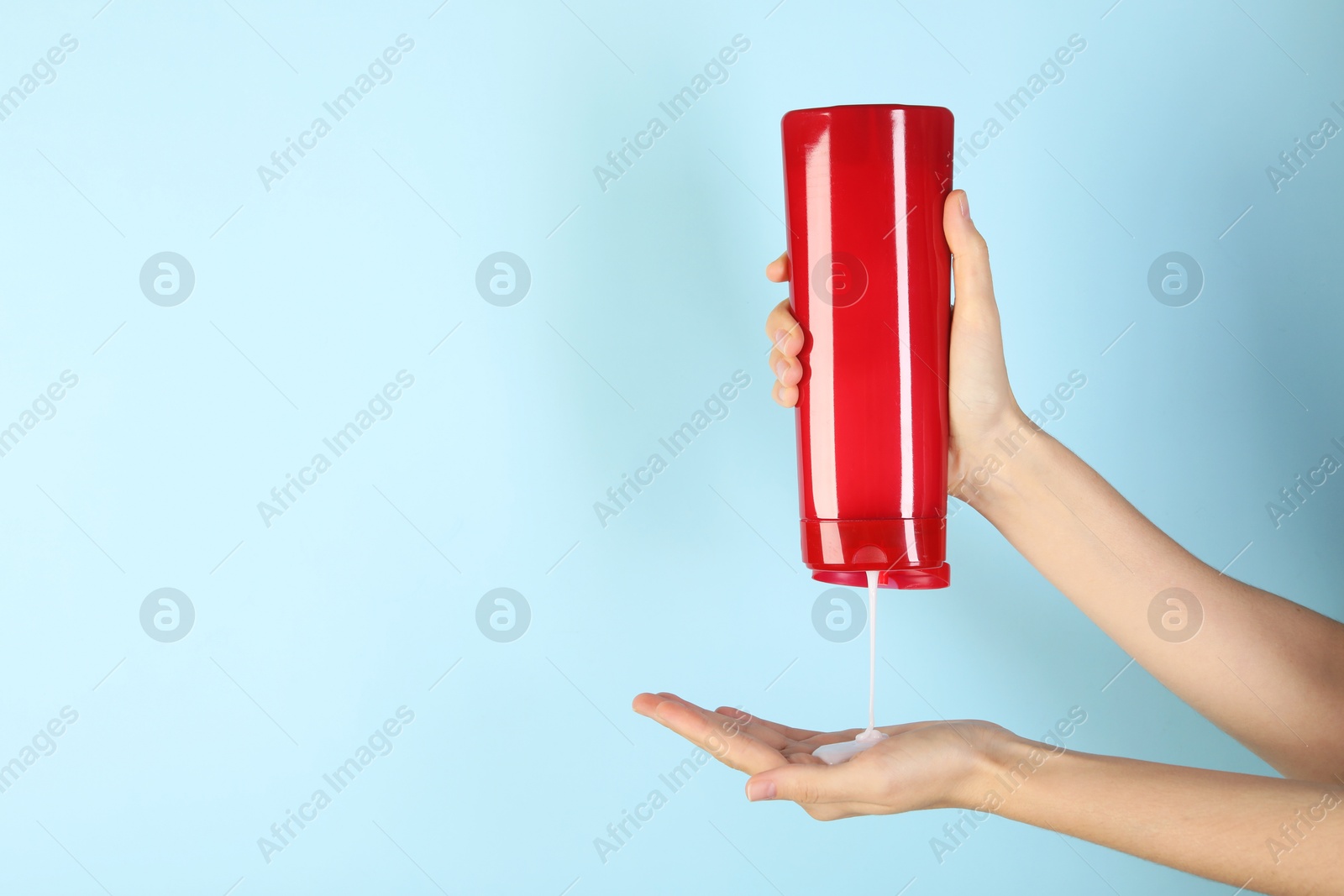 Photo of Woman pouring shampoo onto hand on light blue background, closeup. Space for text