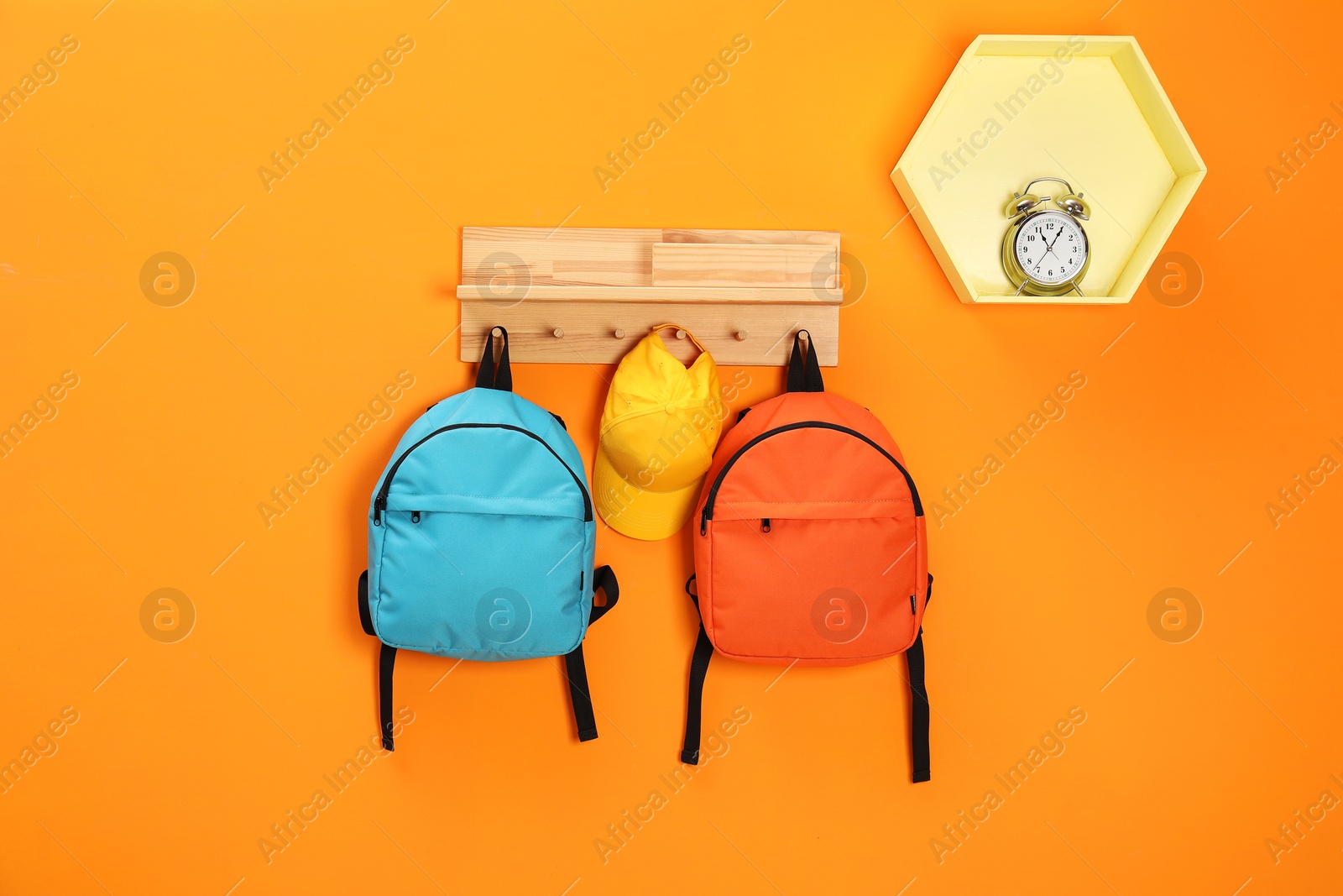 Photo of Bright backpacks, cap and alarm clock on orange wall