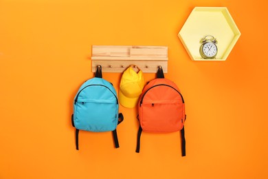 Photo of Bright backpacks, cap and alarm clock on orange wall