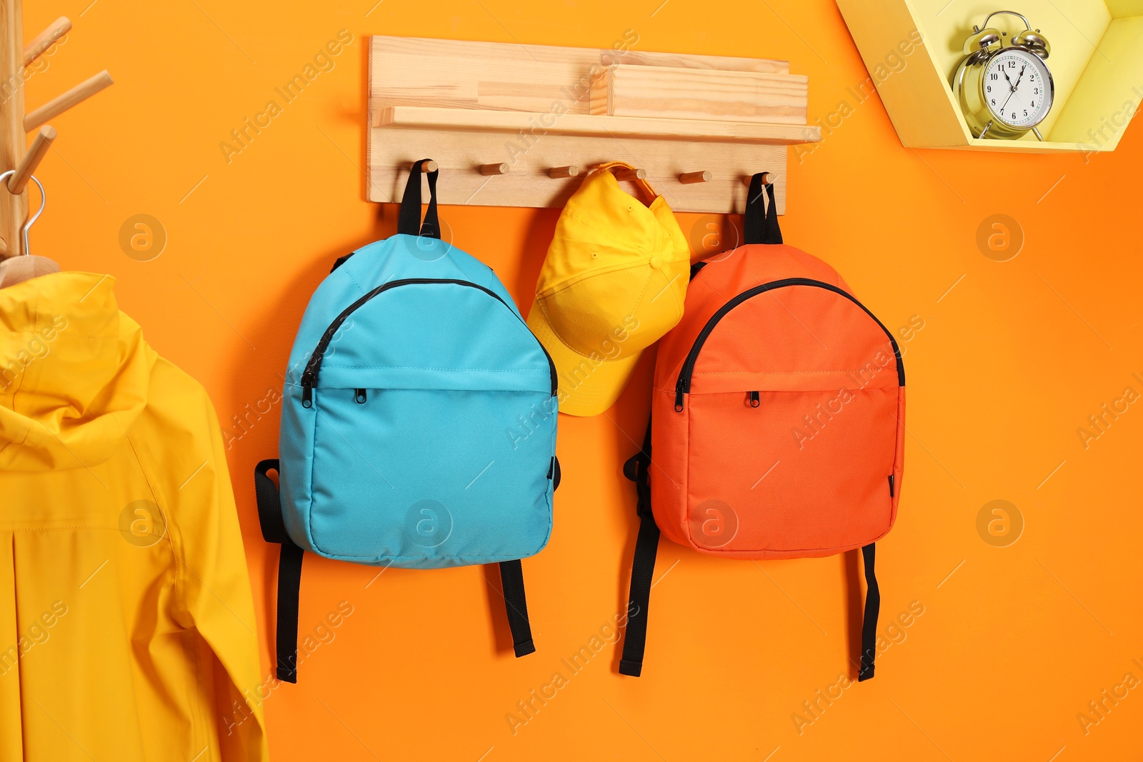 Photo of Bright backpacks, cap, coat and alarm clock near orange wall