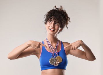 Happy winner pointing at her medals on light grey background