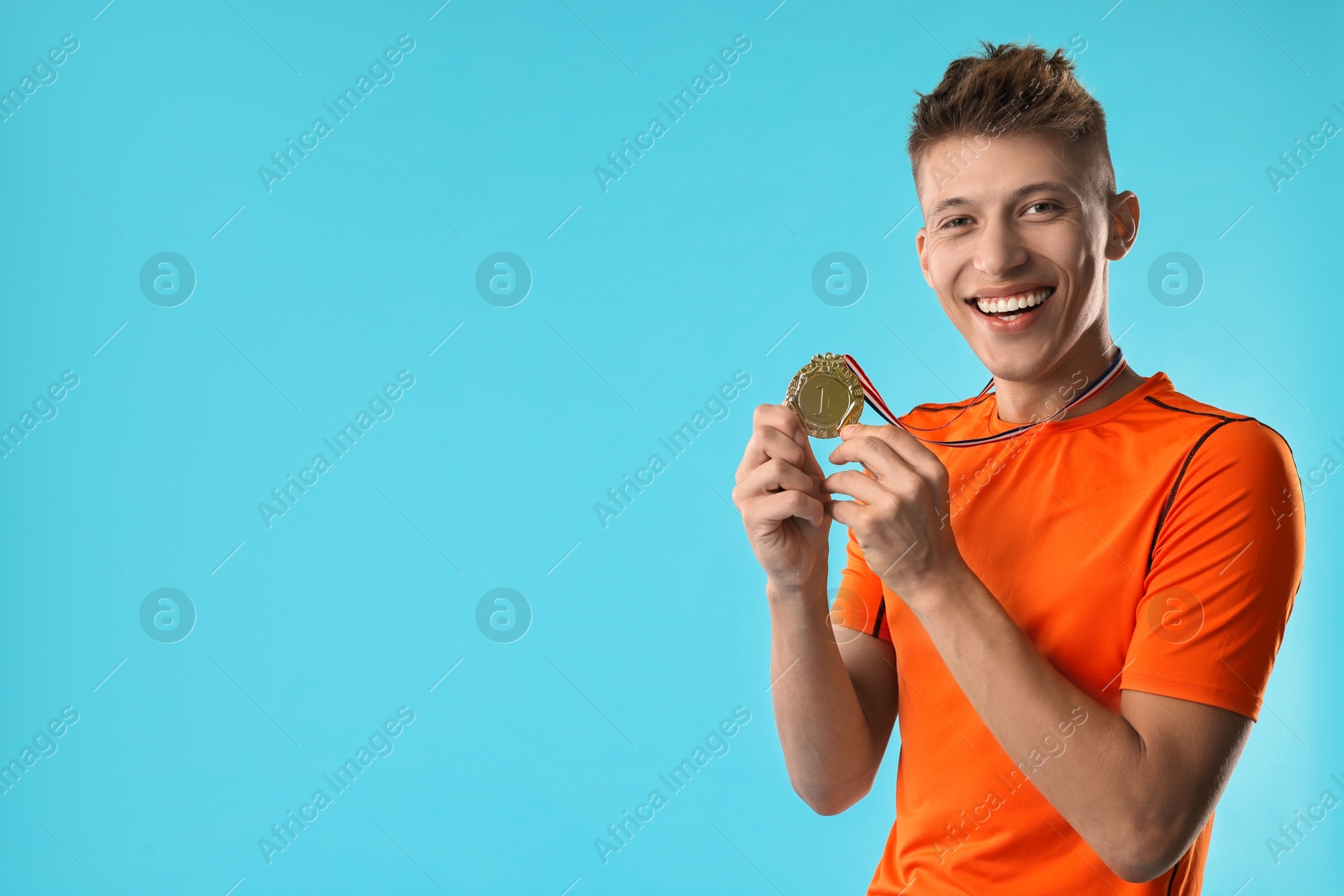 Photo of Happy winner with golden medal on light blue background. Space for text