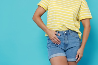 Woman wearing stylish denim shorts on light blue background, closeup. Space for text