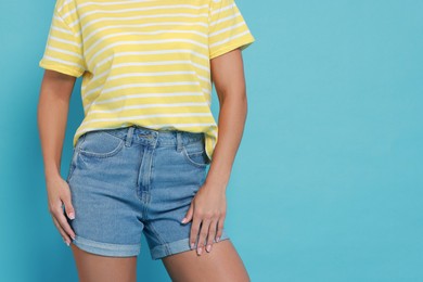 Woman wearing stylish denim shorts on light blue background, closeup. Space for text