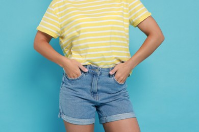 Woman wearing stylish denim shorts on light blue background, closeup