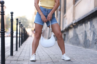 Woman with white bag wearing stylish denim shorts outdoors, closeup