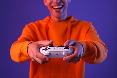 Photo of Man playing video games with controller on violet background, closeup