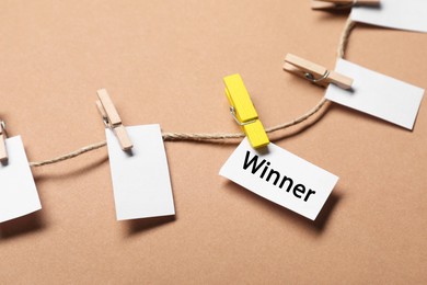 Photo of Paper note with word Winner among blank ones on rope against beige background, closeup