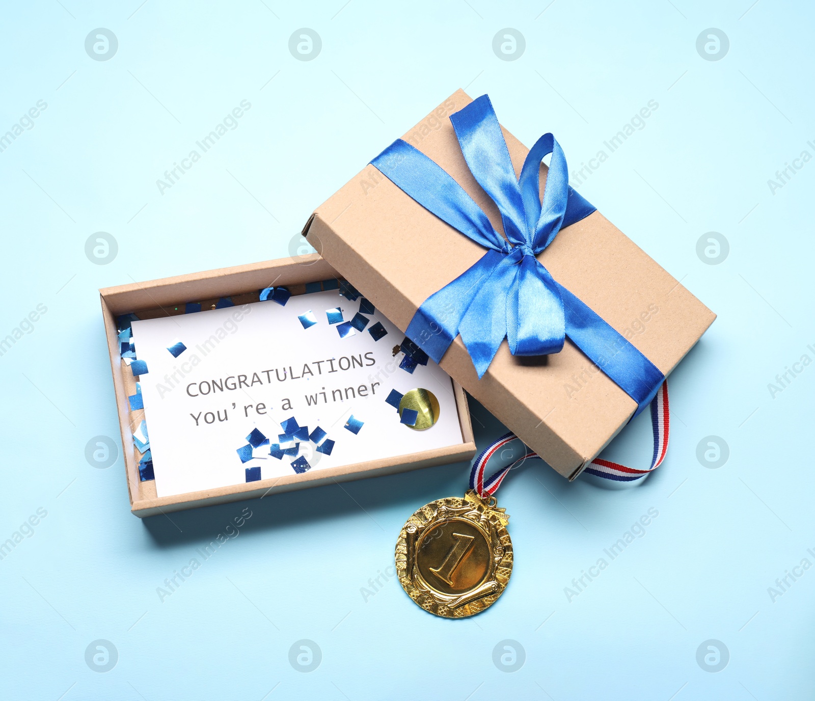 Photo of Card with phrase Congratulations You`re Winner in gift box and golden medal on light blue background, above view