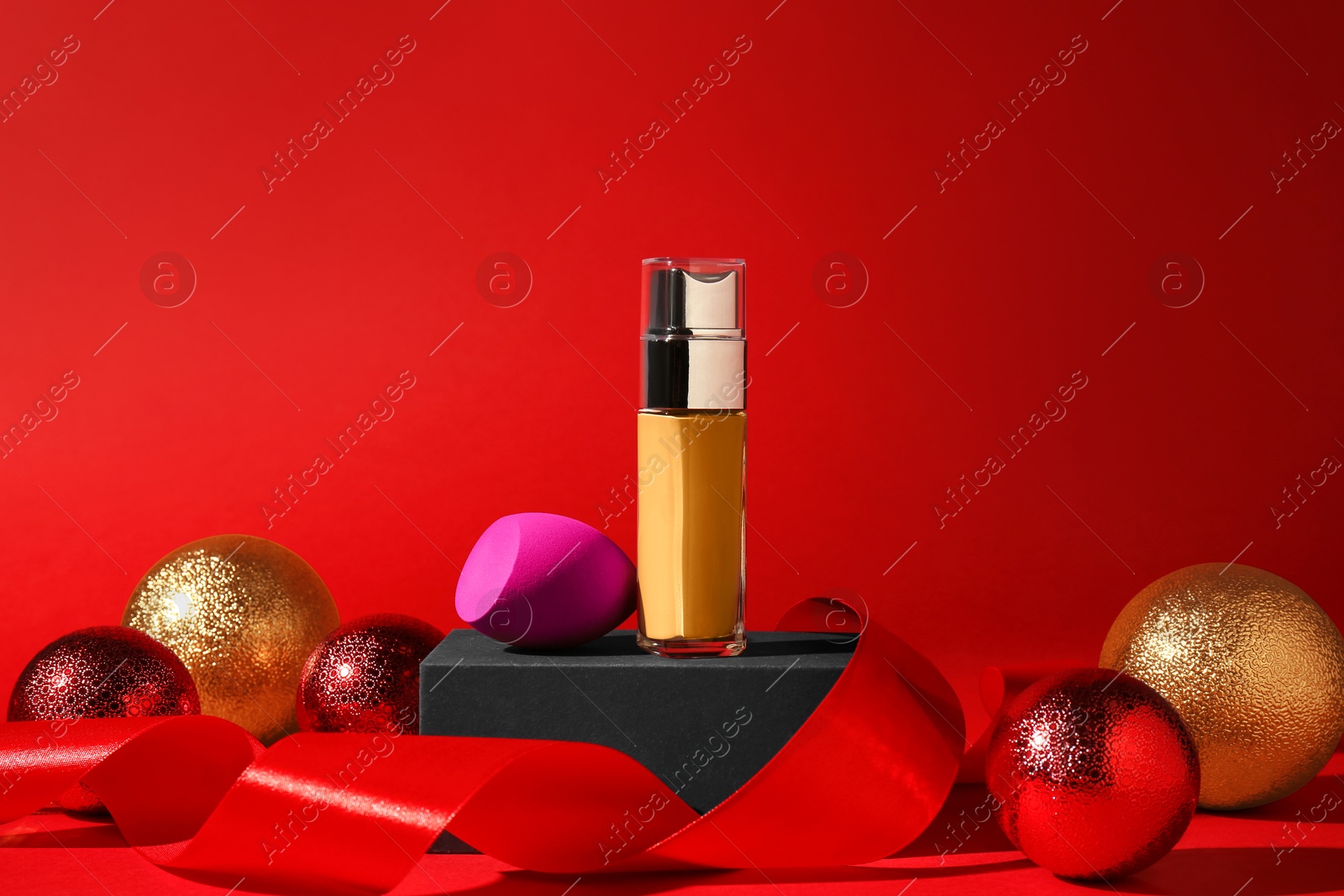 Photo of Christmas present. Liquid foundation, sponge, gift box and festive decor on red background