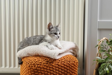 Photo of Cute little kitten on pouf near radiator at home