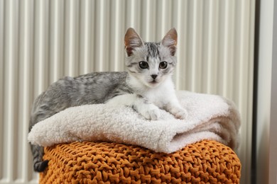 Photo of Cute little kitten on pouf near radiator at home