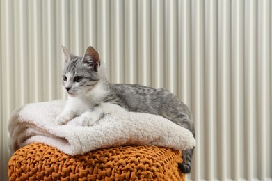 Photo of Cute little kitten on pouf near radiator at home