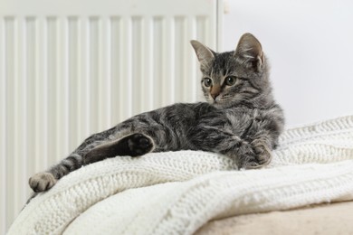 Photo of Cute little kitten on pouf near radiator at home