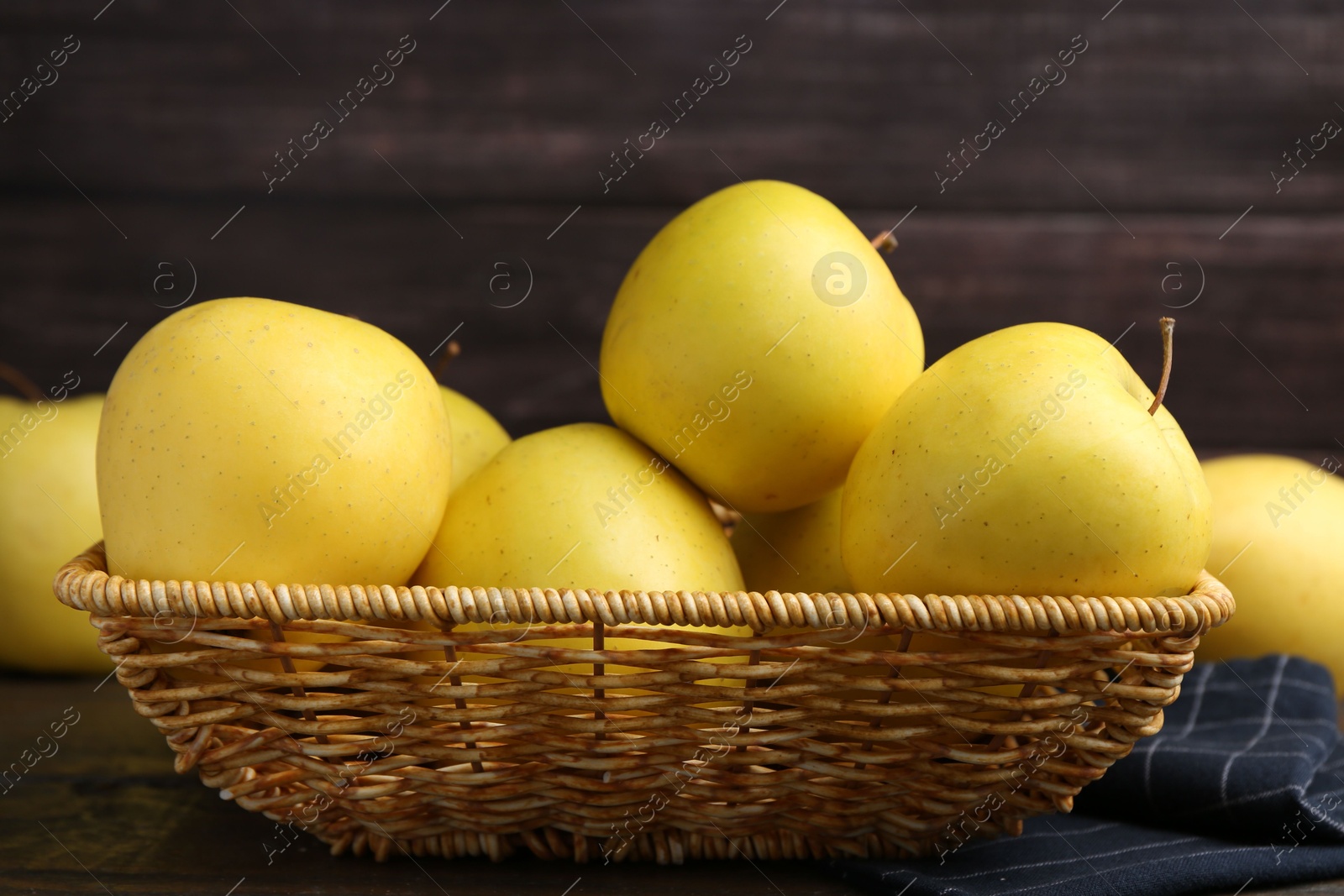 Photo of Fresh yellow apples in wicker basket on table, closeup