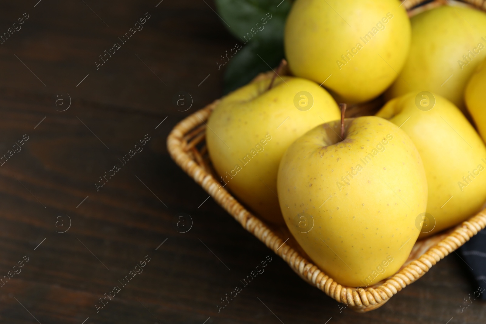 Photo of Fresh yellow apples in wicker basket on wooden table, closeup. Space for text