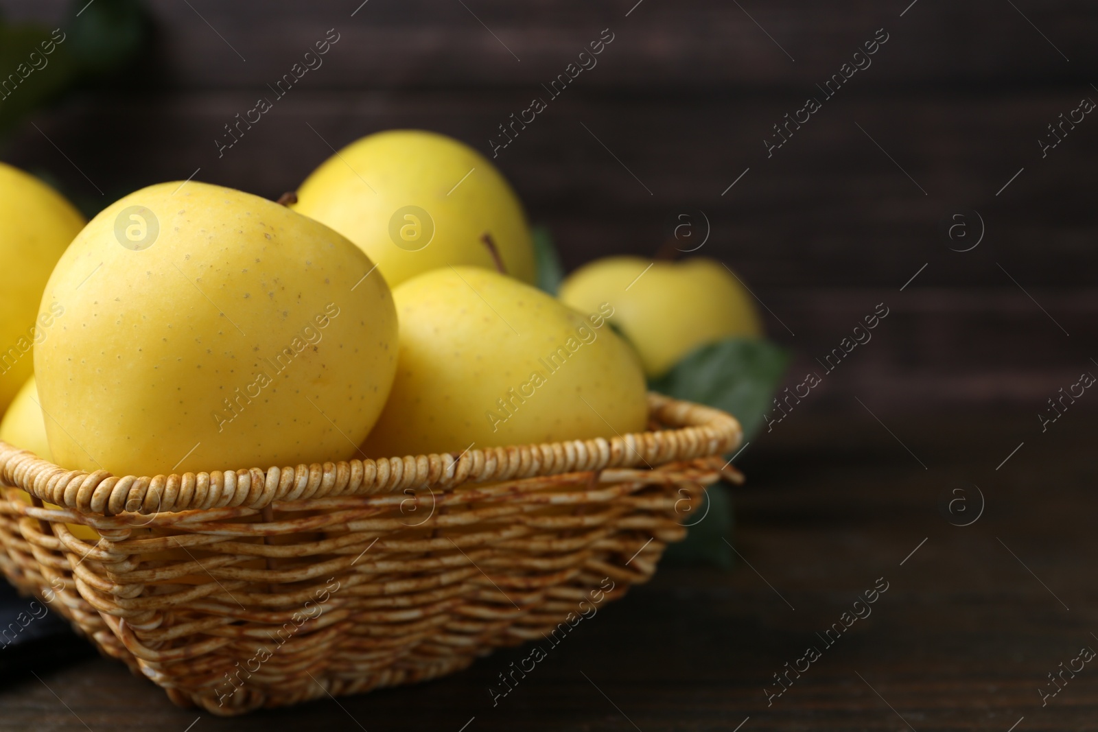 Photo of Fresh yellow apples in wicker basket on wooden table, closeup. Space for text