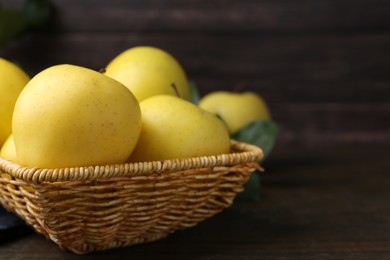 Fresh yellow apples in wicker basket on wooden table, closeup. Space for text