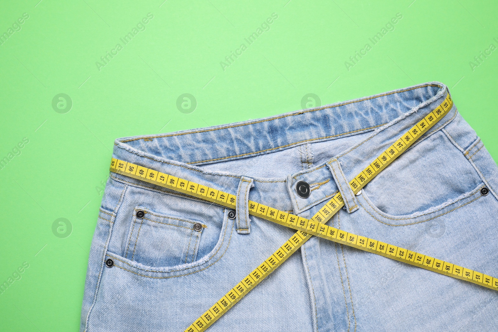 Photo of Jeans and measuring tape on green background, top view