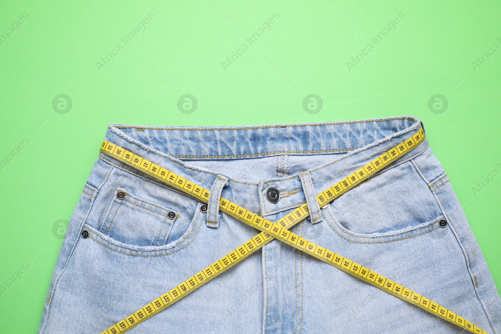 Photo of Jeans and measuring tape on green background, top view