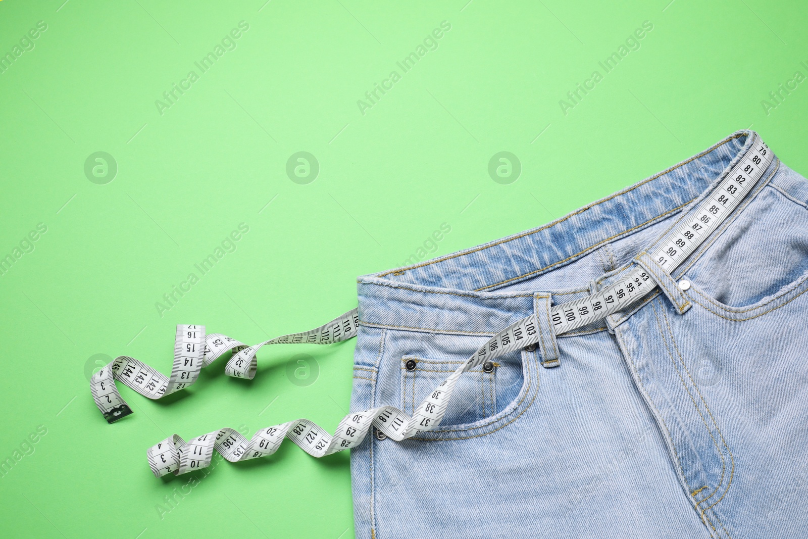 Photo of Jeans and measuring tape on green background, top view