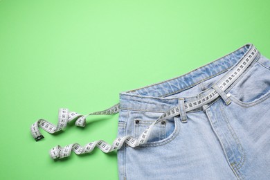 Photo of Jeans and measuring tape on green background, top view