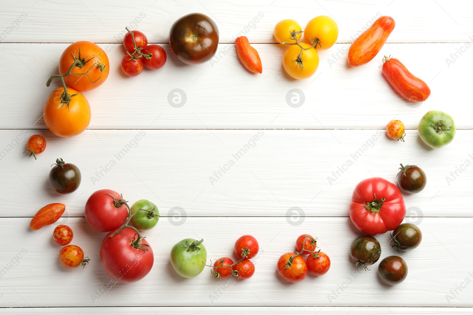 Photo of Frame made of different ripe and unripe tomatoes on white wooden table, flat lay. Space for text