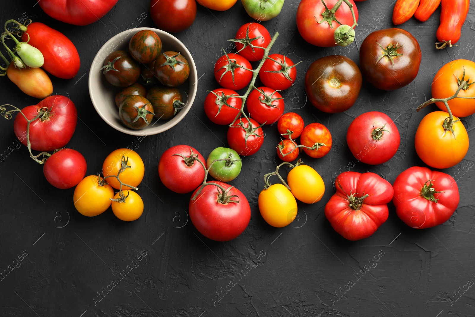 Photo of Different fresh tomatoes on grey textured table, flat lay