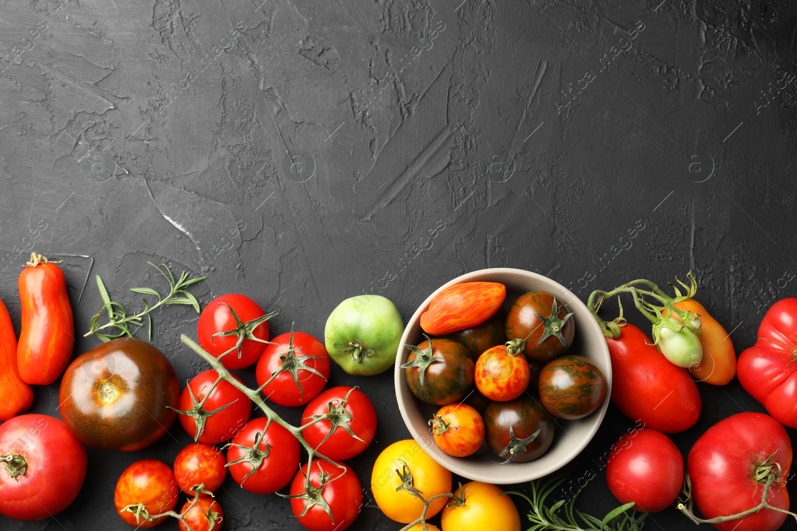 Photo of Different fresh tomatoes and rosemary on grey textured table, flat lay. Space for text