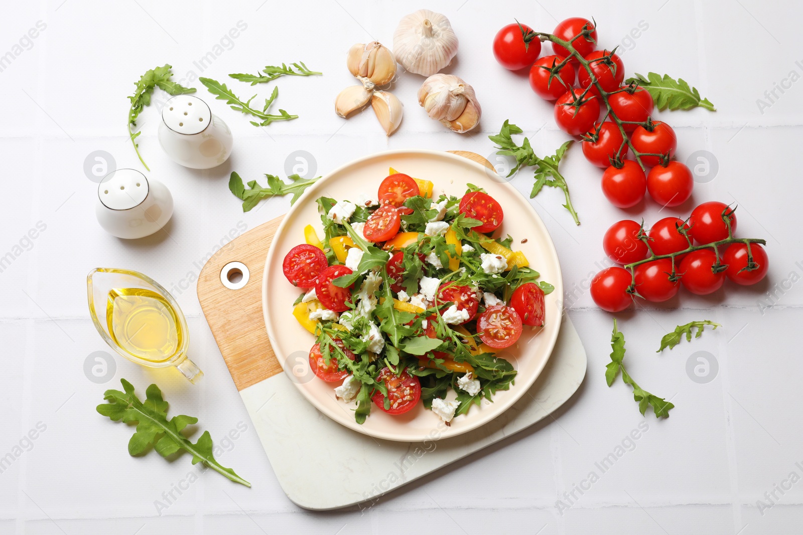 Photo of Tasty salad with arugula, cheese and vegetables on white tiled table, flat lay