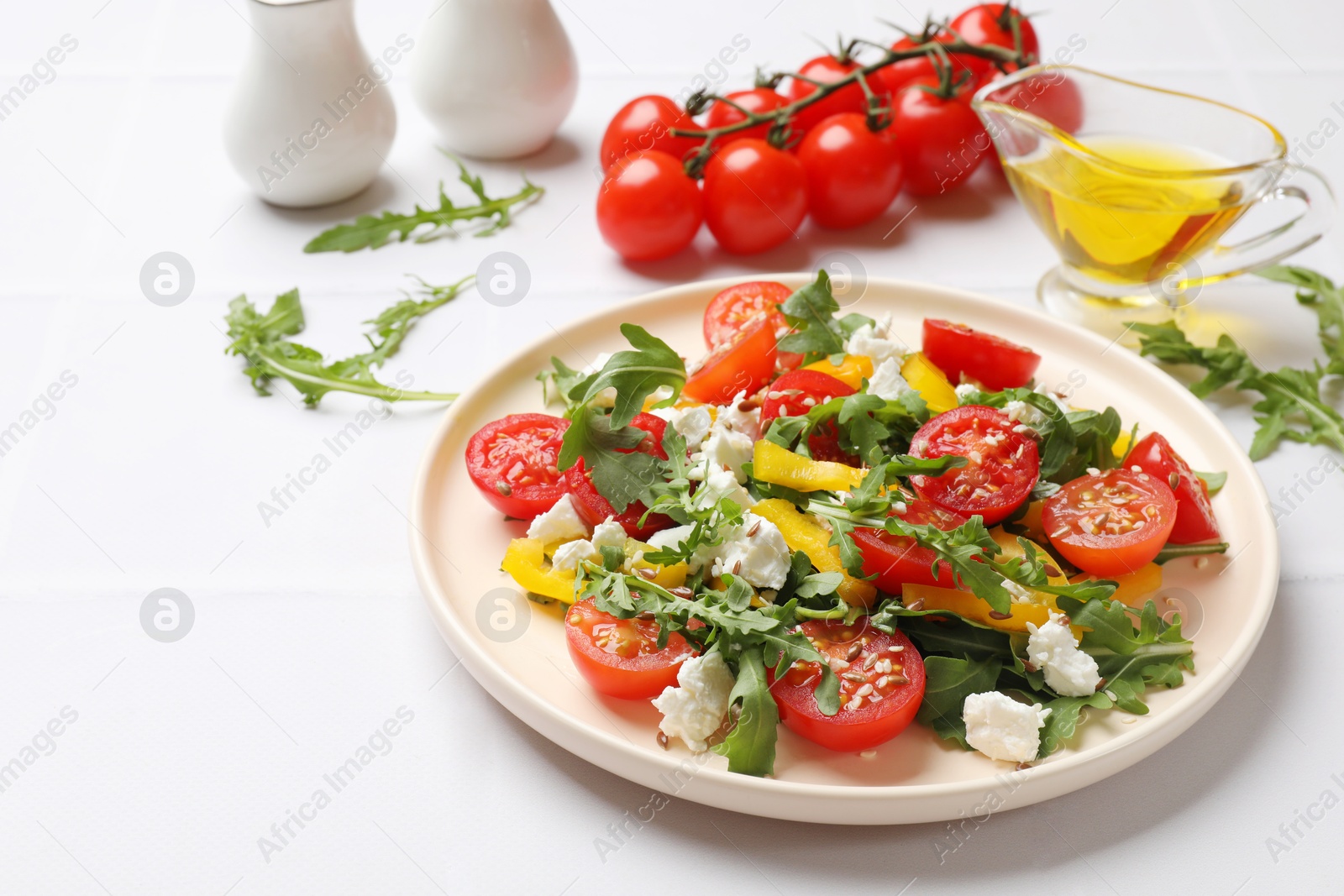 Photo of Tasty salad with arugula, cheese and vegetables on white tiled table