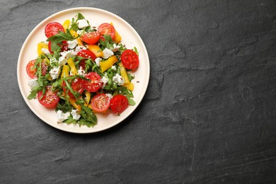 Photo of Tasty salad with arugula, cheese and vegetables on dark textured table, top view. Space for text