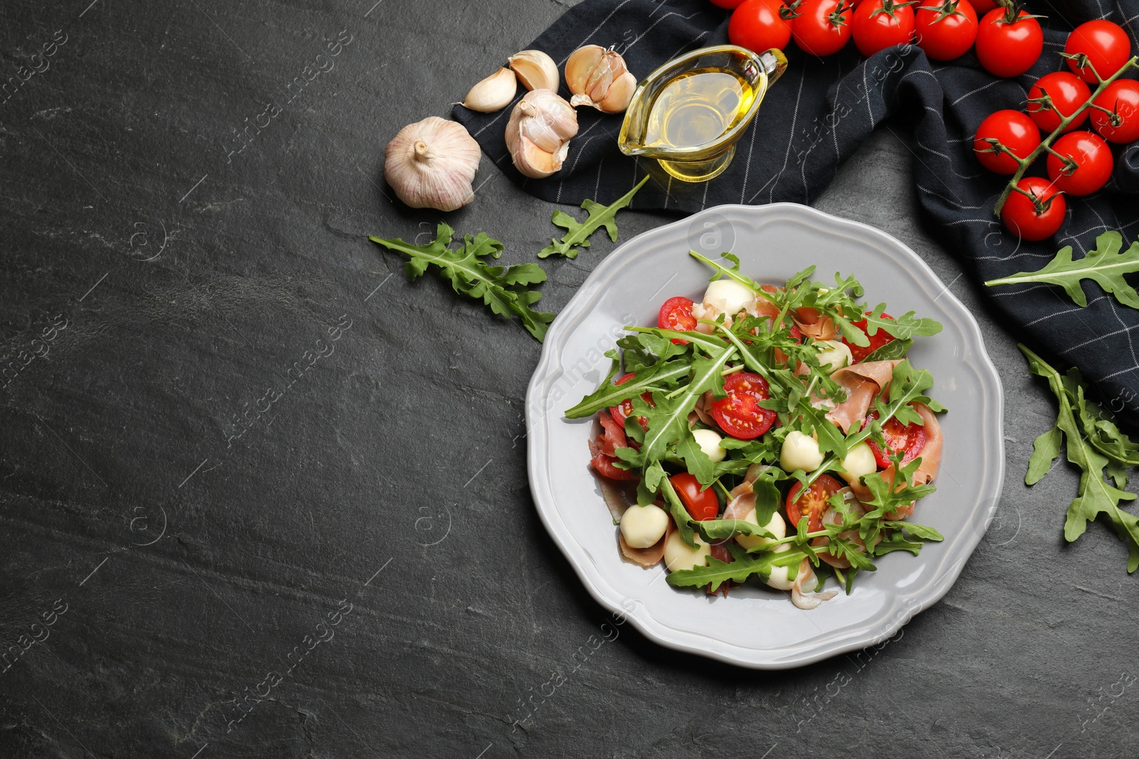 Photo of Tasty salad with arugula, cheese and vegetables on dark textured table, flat lay. Space for text