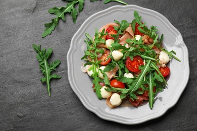 Photo of Tasty salad with arugula on dark textured table, flat lay