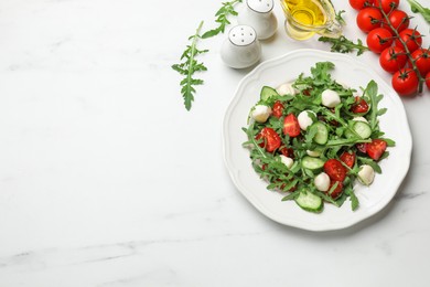 Photo of Tasty salad with arugula, mozzarella, tomatoes and cucumber on white marble table, flat lay. Space for text