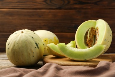 Photo of Fresh whole and cut honeydew melons on wooden table, closeup