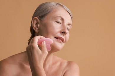 Beautiful woman doing facial massage with gua sha tool on beige background, space for text