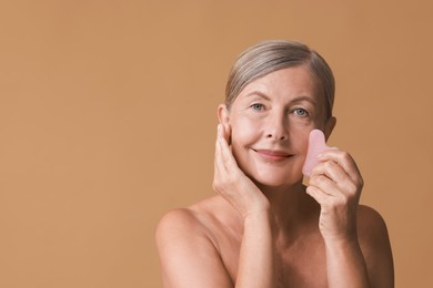 Beautiful woman doing facial massage with gua sha tool on beige background, space for text