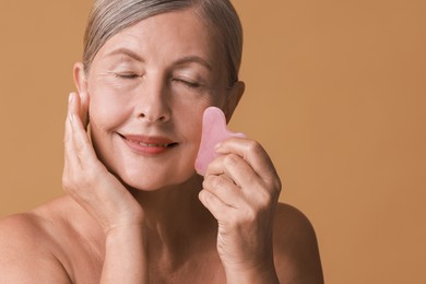 Beautiful woman doing facial massage with gua sha tool on beige background