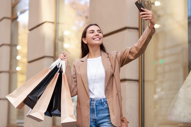 Photo of Happy woman with many shopping bags taking selfie outdoors