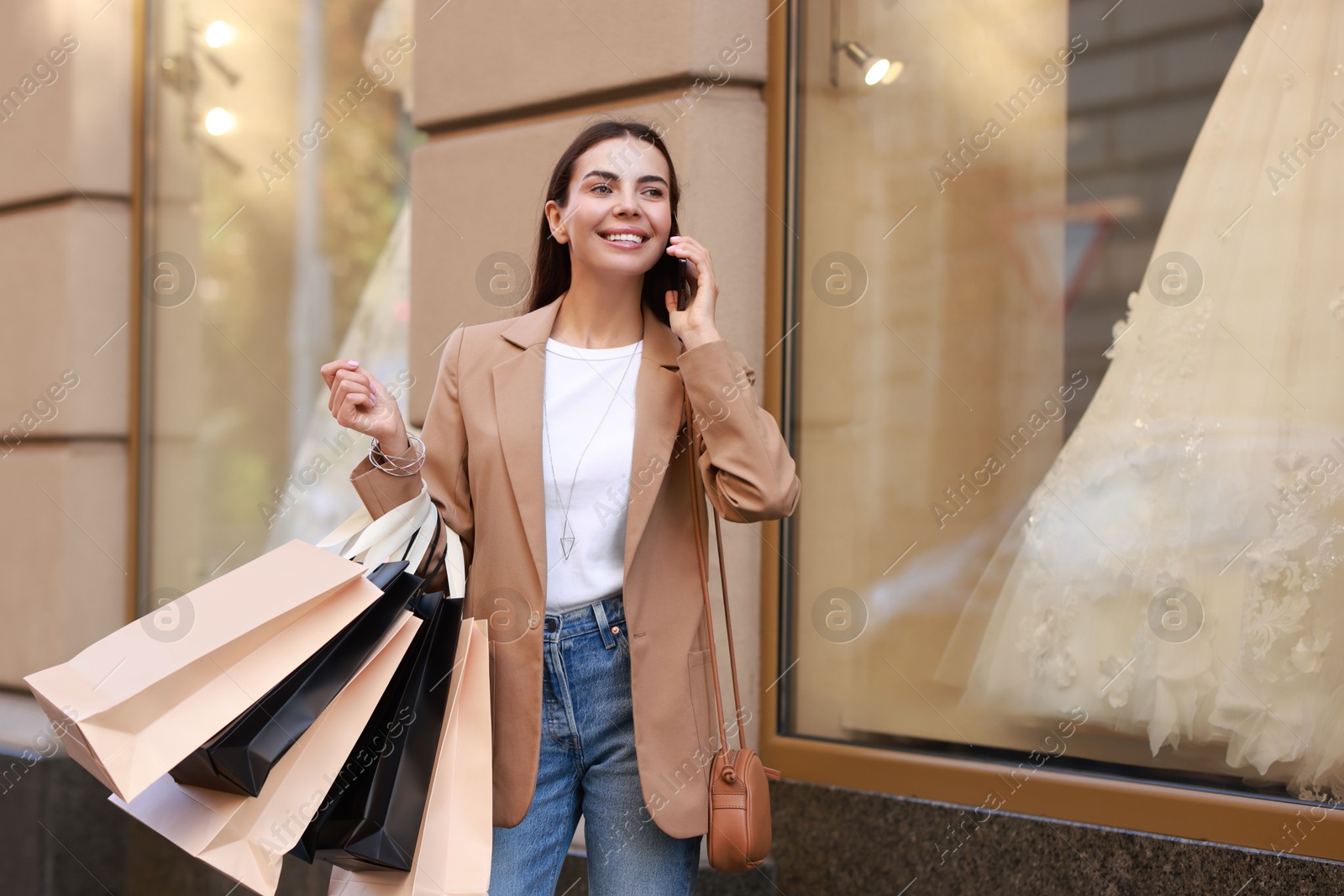 Photo of Happy woman with shopping bags talking on smartphone outdoors