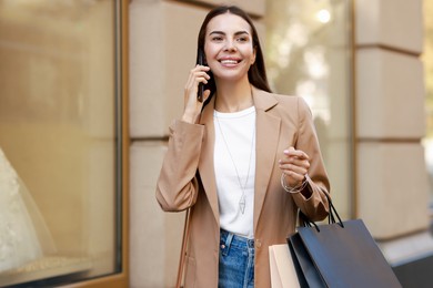 Happy woman with shopping bags talking on smartphone outdoors, space for text