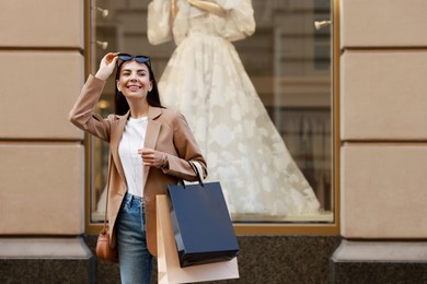 Happy woman with many shopping bags outdoors, space for text