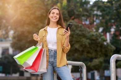 Happy woman with colorful shopping bags using smartphone outdoors